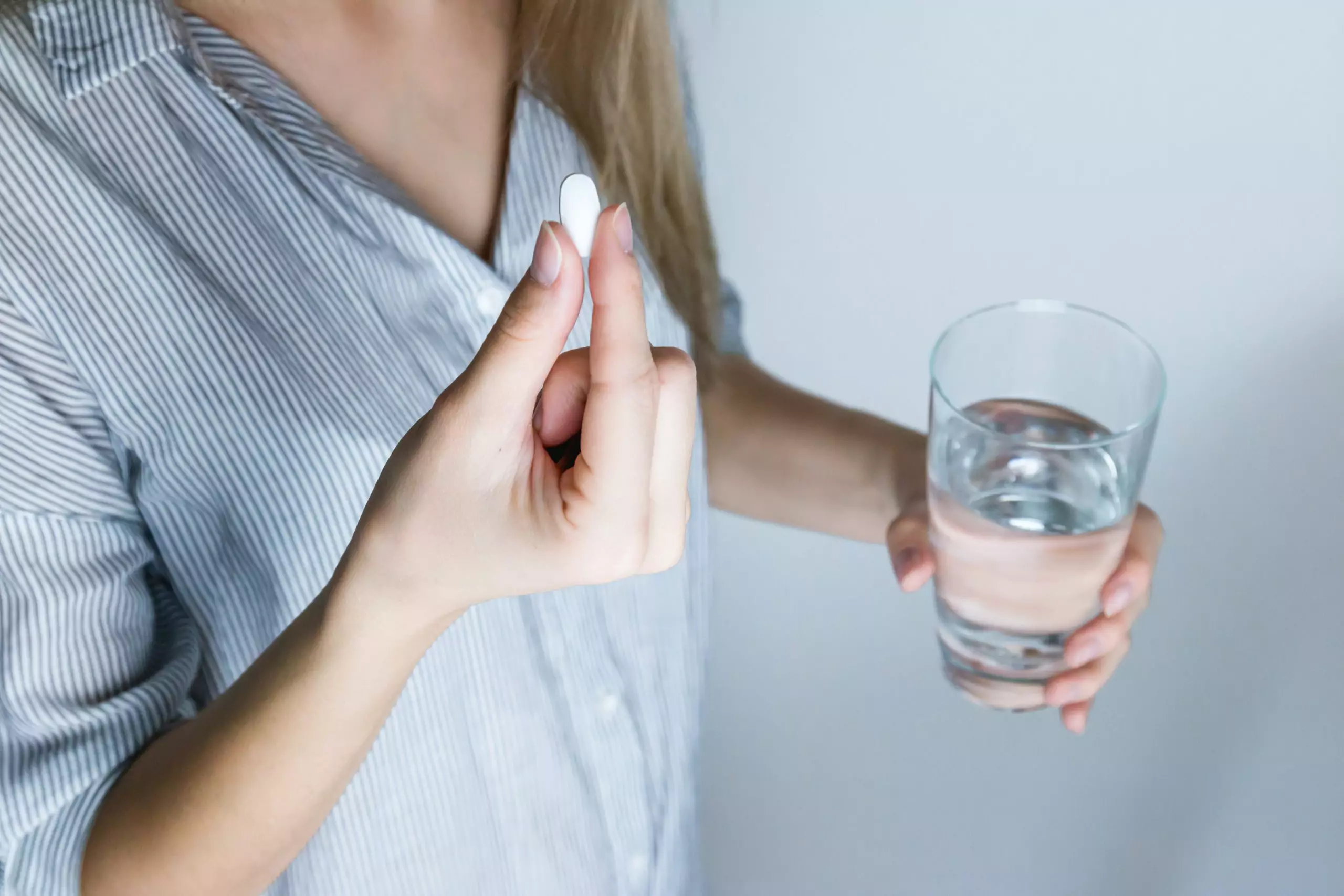 Woman with a pill in one hand and a glass of water in the other