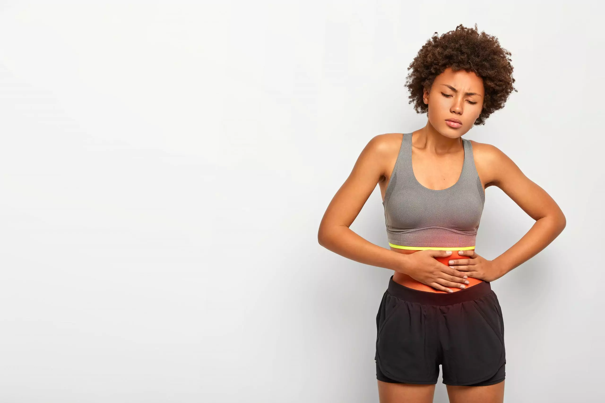 Young black woman in workout gear holding abdomen from pain due to subserosal fibroids