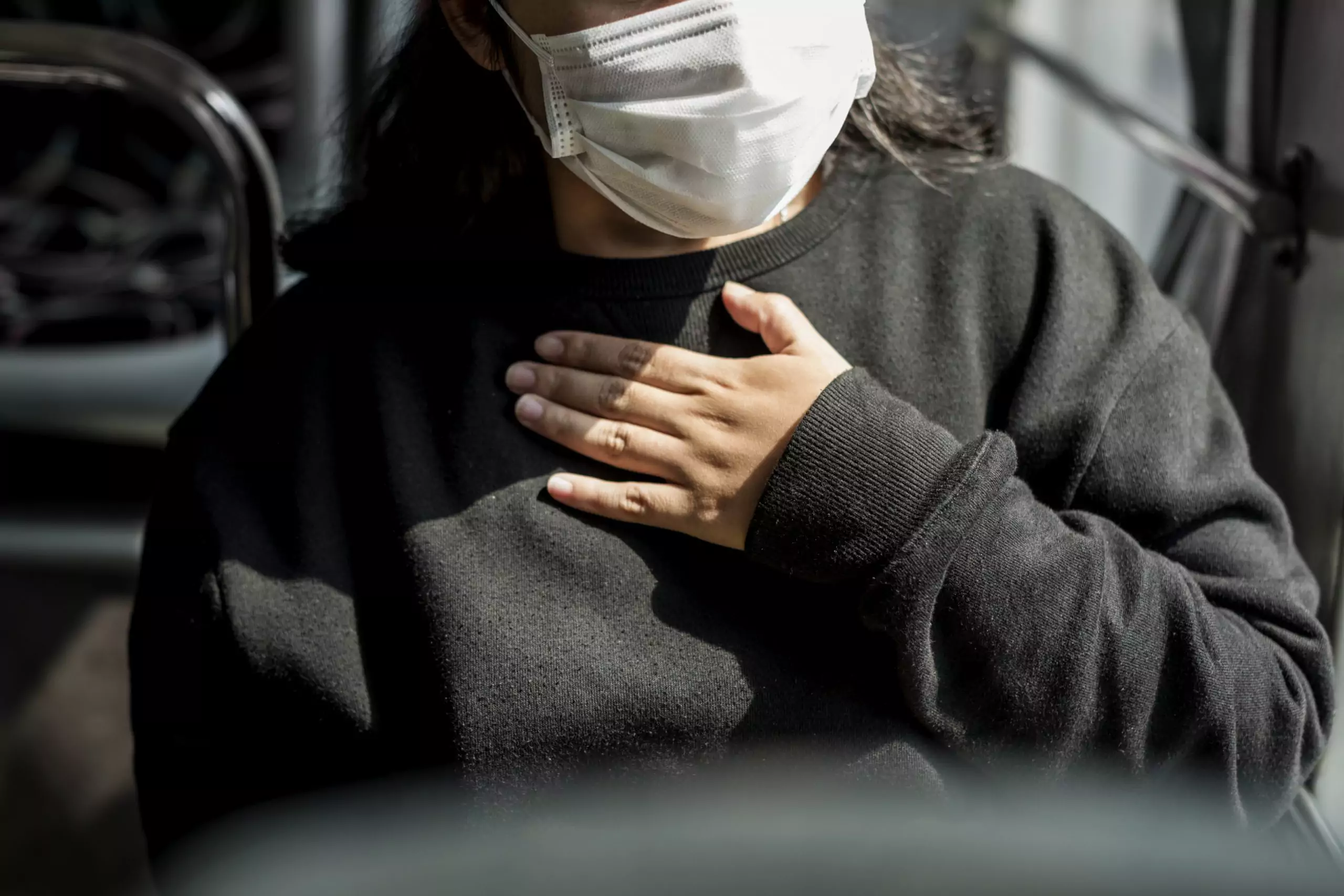 Woman on bus wearing mask and holding chest is a COVID long-hauler